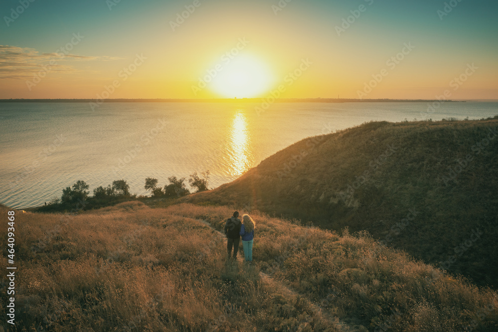 Seascape in an autumn evening. Young couple stands on a hill in the evening and looks at a beautiful sunset
