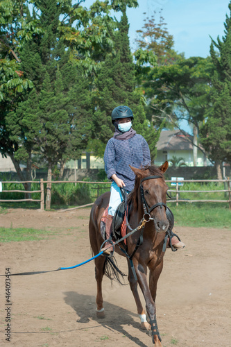 Women with mask and hijab learns to ride a horse. girls riding horses at the ranch. equestrian sport during the pandemic