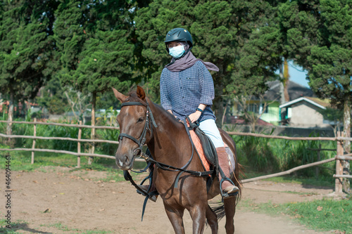 Women with mask and hijab learns to ride a horse. girls riding horses at the ranch. equestrian sport during the pandemic