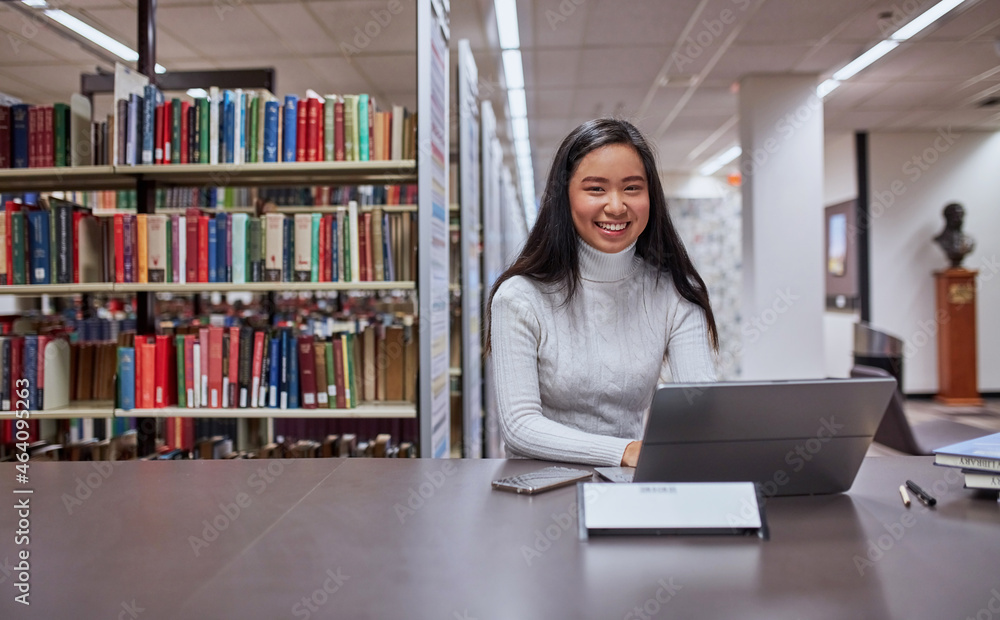 Young female Asian student working on her laptop at university library ...