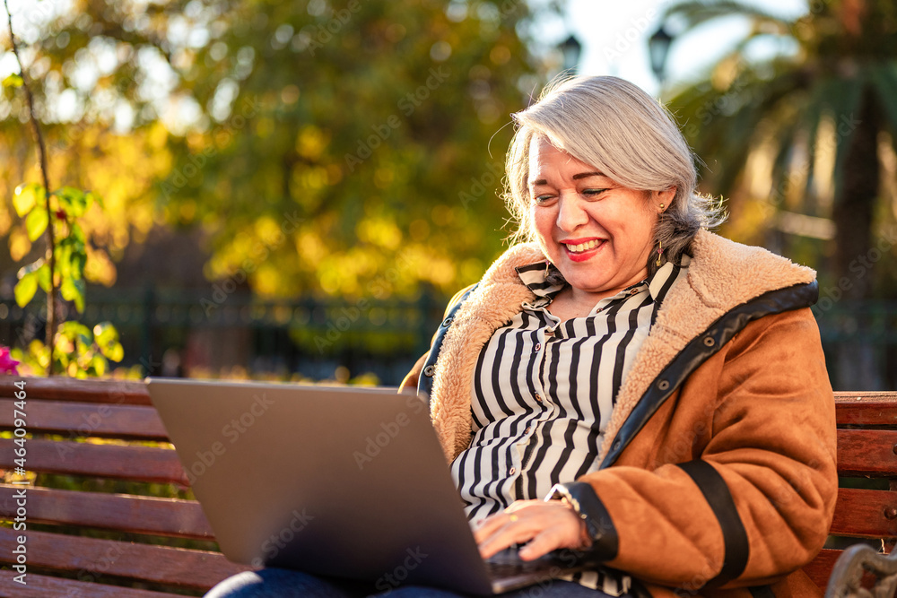 Mature woman smiling using a computer laptop at the park Mature woman smiling using a computer laptop at the park