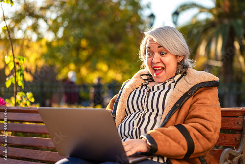 Mature woman smiling using a computer laptop at the park photo