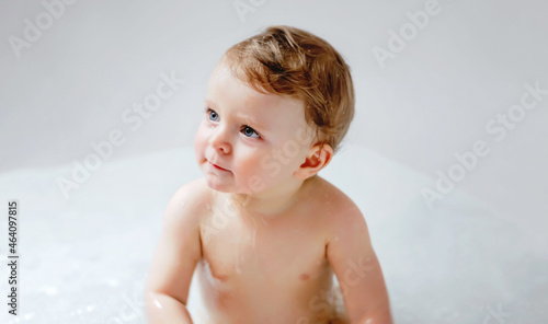 Cute adorable baby child taking bath in bathtub at home. Happy healthy boy or girl playing, splashing and having fun during bathtime. Hygiene and cleaning concept for babies.