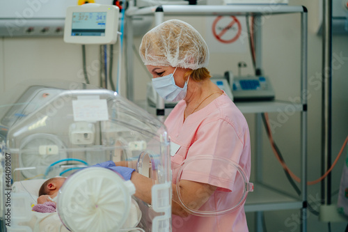 At the intensive care unit. Nurse standing near hospital bed with a baby preparing it for treatment. Newborn is placed in the incubator. Neonatal intensive care unit photo