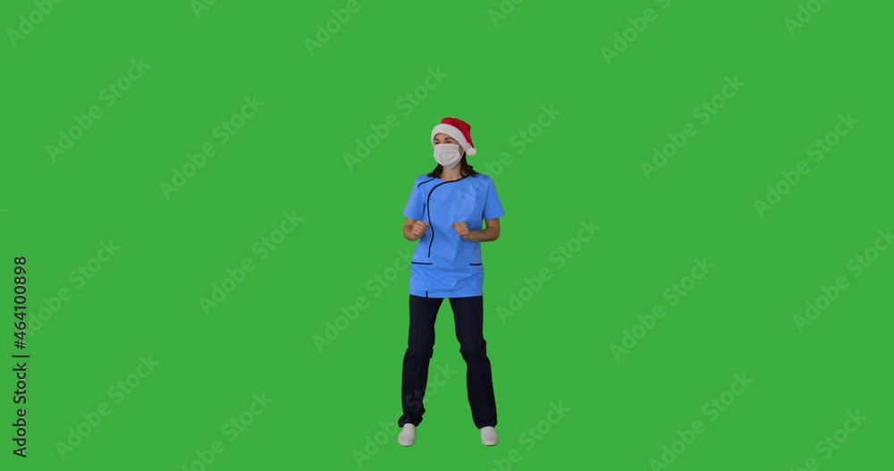 Frontline healthcare worker dancing in santa hat wearing protective face mask over green background Frontline healthcare worker dancing in santa hat wearing protective face mask over green background