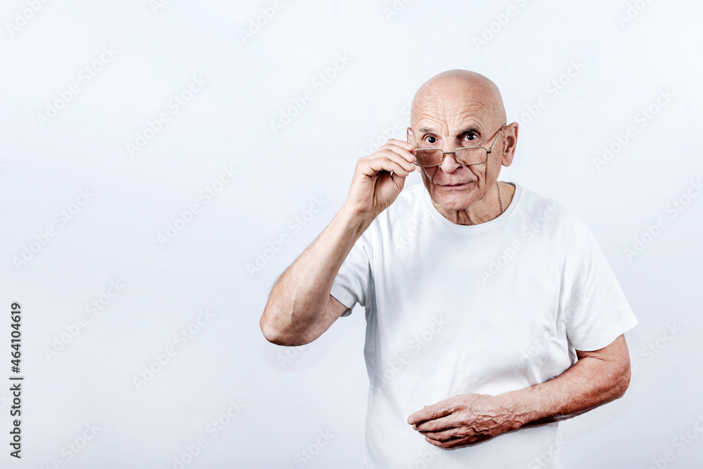 Mature bald man looking from under glasses touching frames