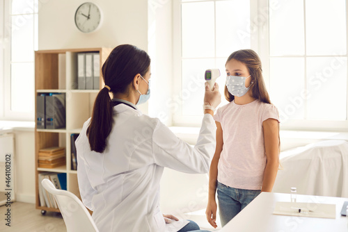 Doctor or nurse using modern infrared thermometer and pointing it at little kid's forehead. Child who's wearing face mask gets body temperature checked at clinic. Covid 19, health and safety concept