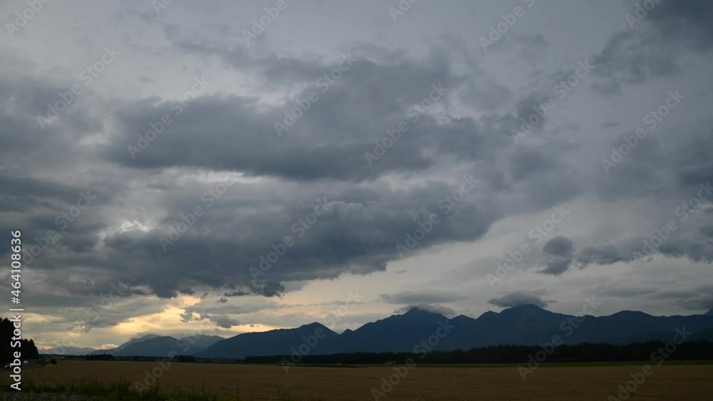 Time lapse of dramatic clouds moving over beautiful landscape in Slovenia. Farmland in the foreground, mountains in the distance. Summer sunset. Static shot Time lapse of dramatic clouds moving over beautiful landscape in Slovenia. Farmland in the foreground, mountains in the distance. Summer sunset. Static shot