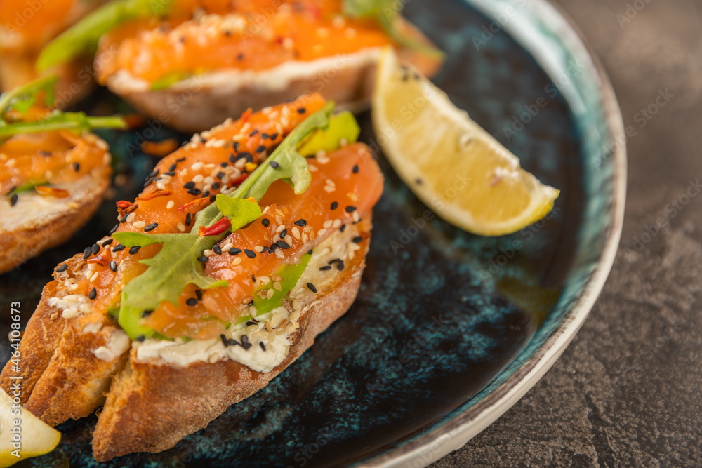 delicious bruschetta with salmon avocado and arugula on a large blue plate. delicious bruschetta with salmon avocado and arugula on a large blue plate.