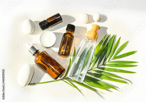 bottles and dispensers with natural cosmetics or oils on white background and tropical leaf