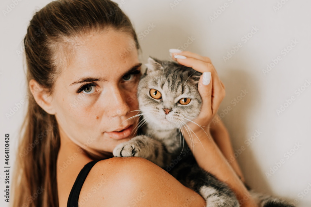 Attractive young woman with long hair embracing her pet with smile. Indoor portrait of cute woman playing with cat. Breed british fold. Healthy lifestyle, harmony and pet. Attractive young woman with long hair embracing her pet with smile. Indoor portrait of cute woman playing with cat. Breed british fold. Healthy lifestyle, harmony and pet.