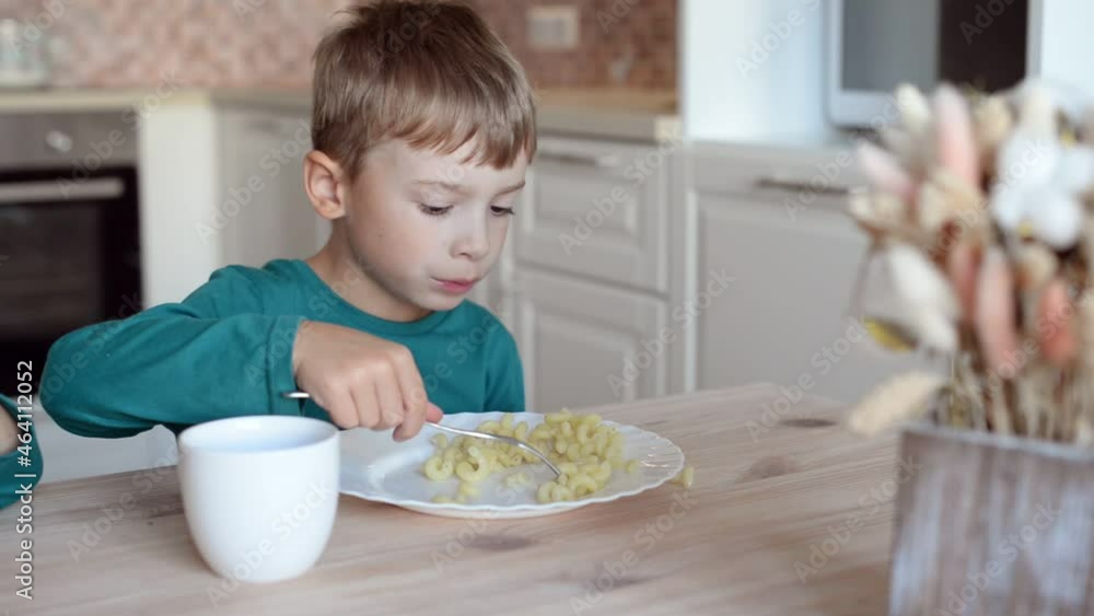 A child with appetite eats pasta while sitting in the kitchen at home. A child with appetite eats pasta while sitting in the kitchen at home.