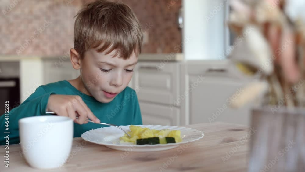 Children nutrition concept. A boy eats boiled potatoes from a white round plate, sitting at a wooden table at home in the kitchen Children nutrition concept. A boy eats boiled potatoes from a white round plate, sitting at a wooden table at home in the kitchen