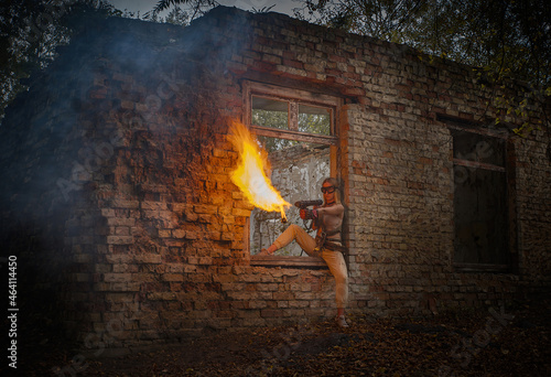 Tableau sur toile A girl in a military uniform with a flamethrower against the background of an old brick building