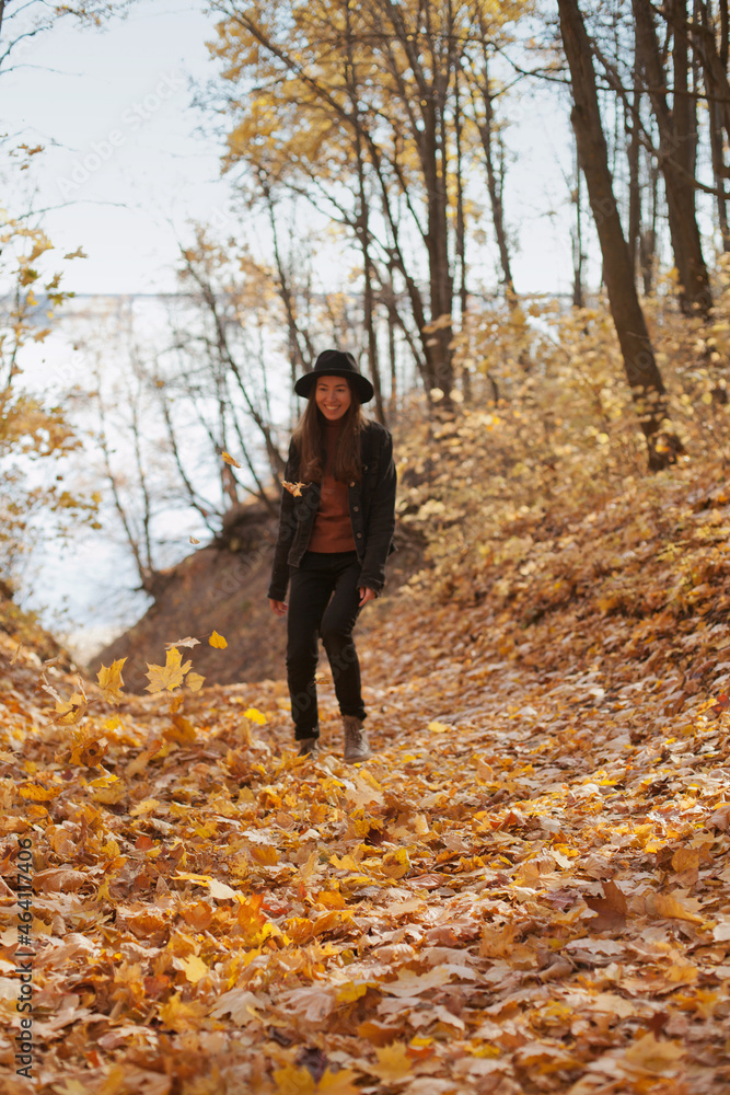 Young woman in black hat having fun in autumn park, throwing fallen autumn leaves in the air