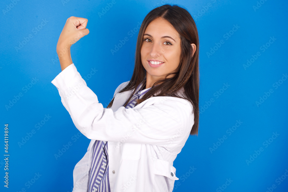 Portrait of powerful cheerful young european doctor girl wearing white medical gown on white background showing muscles. Portrait of powerful cheerful young european doctor girl wearing white medical gown on white background showing muscles.