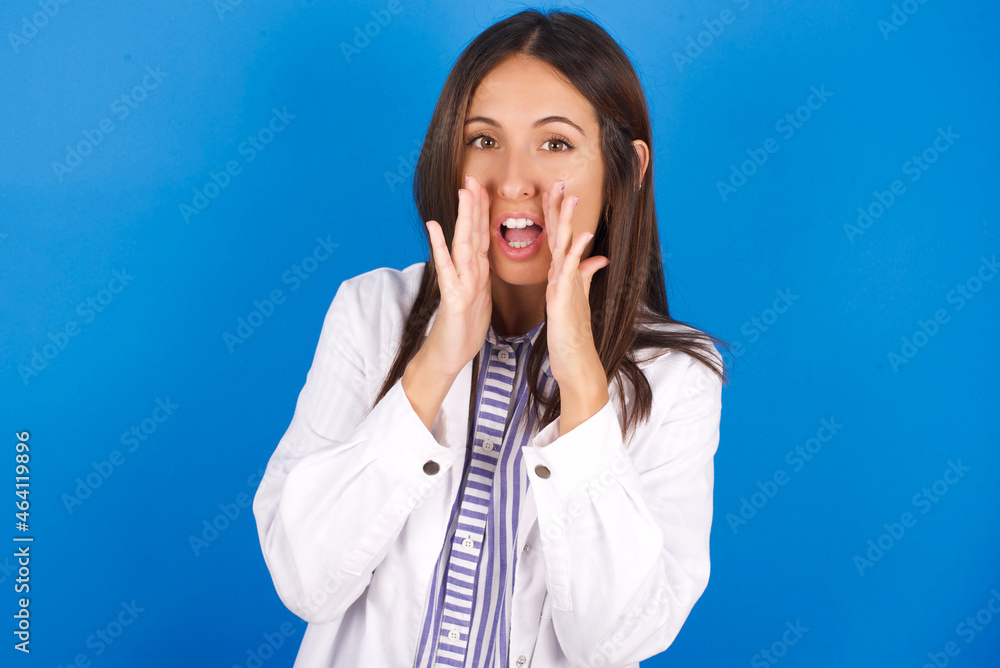 young european doctor girl wearing white medical gown on white background shouting excited to front. young european doctor girl wearing white medical gown on white background shouting excited to front.