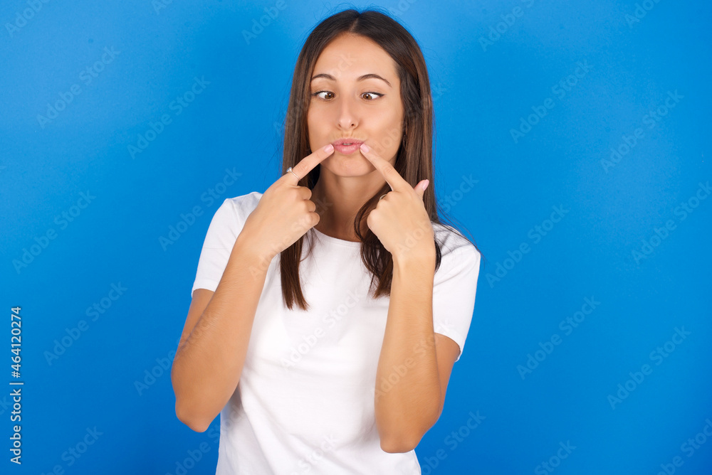 young european girl wearing white t-shirt on white background crosses eyes and makes fish lips funny grimace young european girl wearing white t-shirt on white background crosses eyes and makes fish lips funny grimace