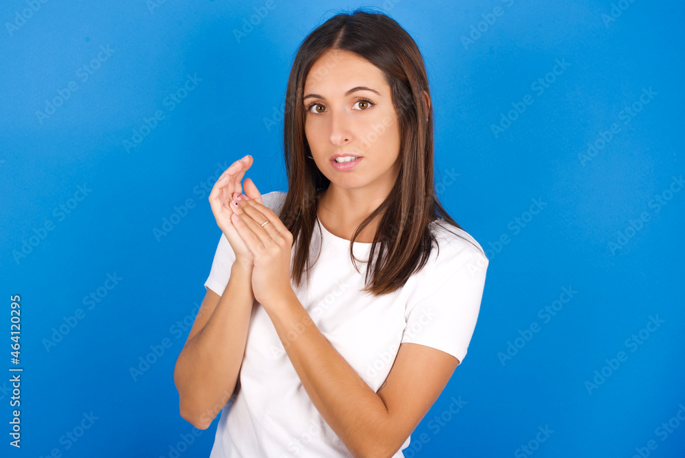 Surprised emotional young european girl wearing white t-shirt on white background rubs palms and stares at camera with disbelief Surprised emotional young european girl wearing white t-shirt on white background rubs palms and stares at camera with disbelief