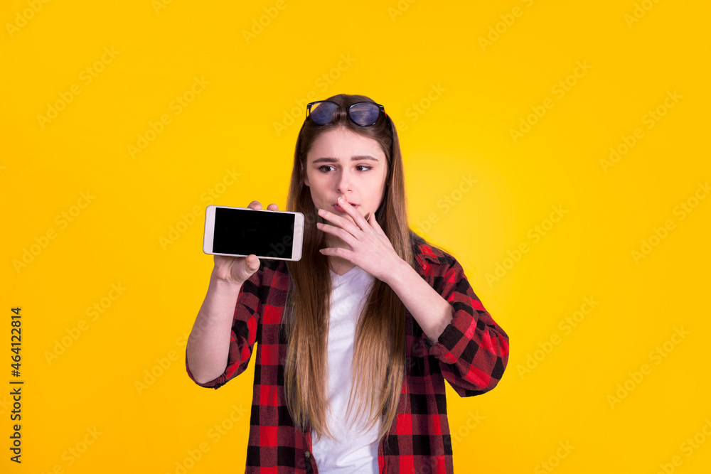Beautiful girl showing phone in a red shirt on a yellow background Beautiful girl showing phone in a red shirt on a yellow background