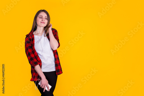 Beautiful fascinating girl in a red shirt listening to music on a yellow background 