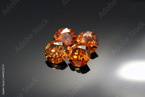 Natural precious zircon gemstones lot. Attractive vibrant golden brown cognac color transparent round faceted clean gemstone settings for making jewelry. Dark gradient background. Gemology theme. photo