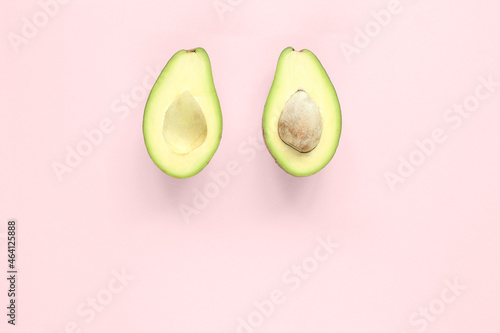 Two halfs of avocado with and without seed on pink background. Top view.