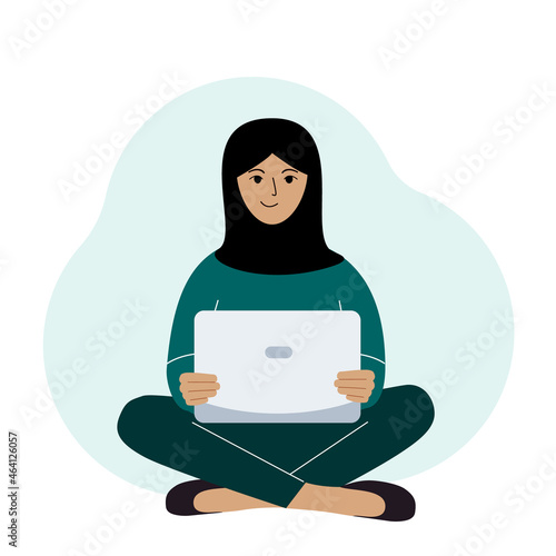 A woman in a black headscarf sits and works at a laptop. Muslim. Remote work or communication over the Internet.