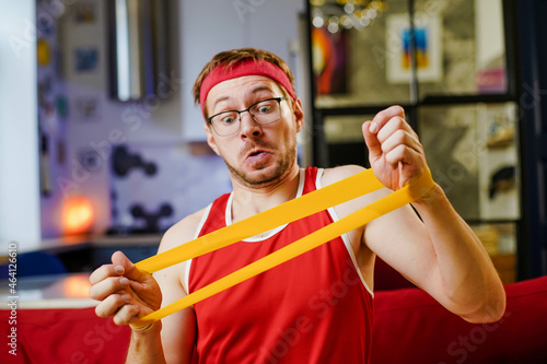 Portrait of funny man in red retro sportswear doing exercises with an elastic resistance band at home Fototapet