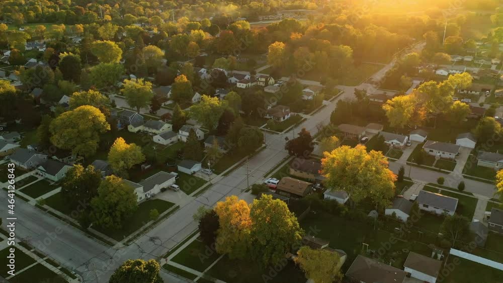 Sunset highlights autumn neighborhood scene with homes and colorful trees along the street, aerial drone shot