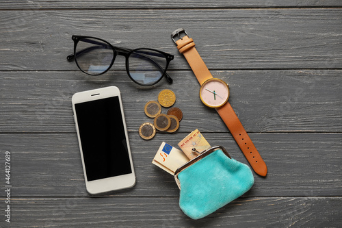Wallet with money, mobile phone, eyeglasses and wristwatch on dark wooden background
