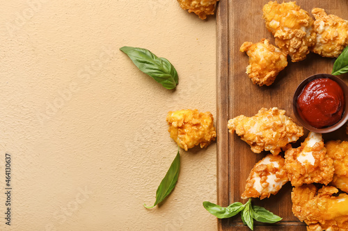 Board with tasty popcorn chicken, sauce and basil on color background