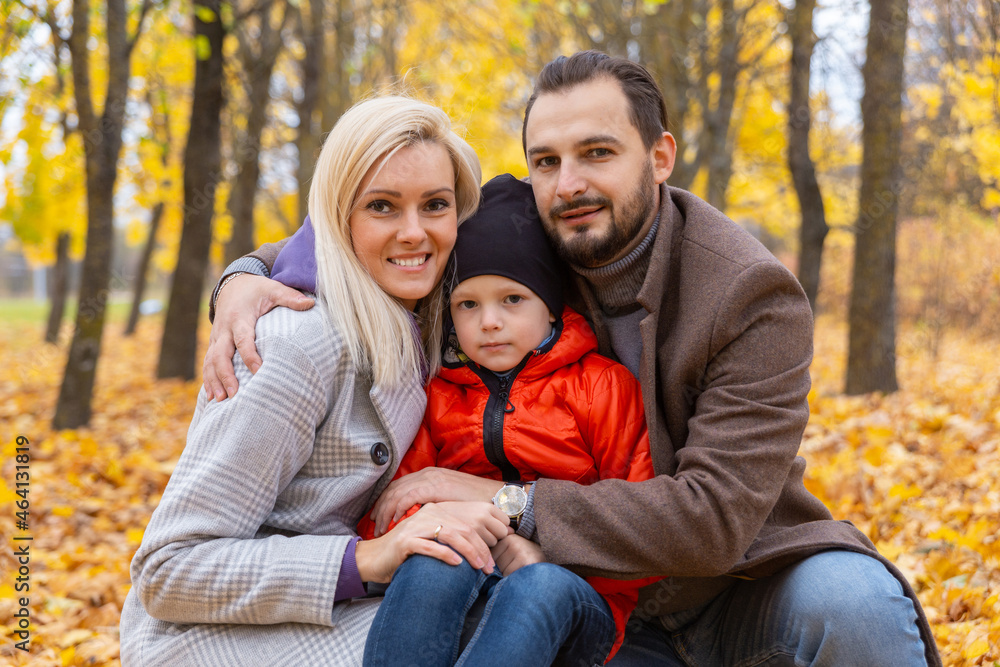 Happy family sitting on dry leaves and looking at camera