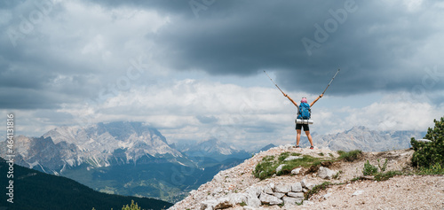 Woman trekker with backpack rose arms up with trekking poles enjoying picturesque Dolomite Alps view near Tre Cime di Lavaredo formation in South Tyrol, Italy. Active people and mountain concept.