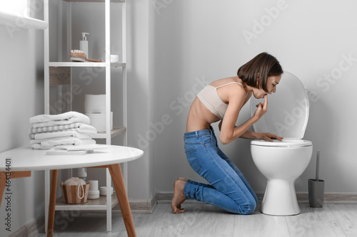 Young woman near toilet bowl in bathroom. Anorexia concept photo