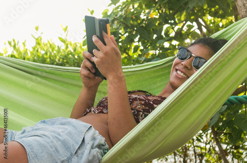Tableau sur toile Beautiful dark-skinned woman reads in a hammock by the ocean