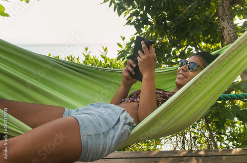 Beautiful dark-skinned woman reads in a hammock by the ocean