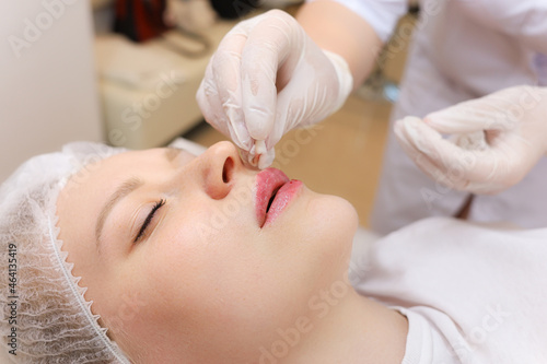 The cosmetologist rubs the girl's lips with oil for care after the lip augmentation procedure with hyaluronic acid