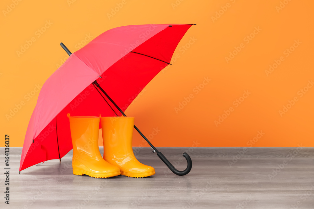 Rubber rain boots with umbrella on floor near color wall - obrazy, fototapety, plakaty 
