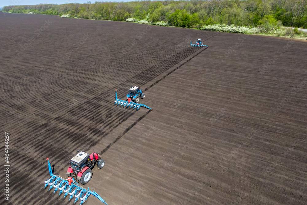 three tractors in the field seeding, sowing crops at field. process of planting seeds in the ground. spring time agricultural activities. Drone photo