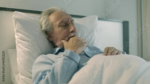 Old man coughing, lying in bed, shortness of breath, symptom of bronchitis photo