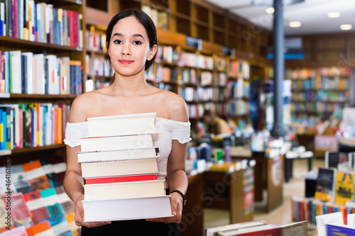 Smiling positive glad attractive girl holding pile of books bought in bookstore