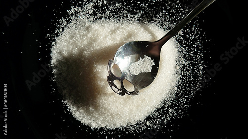Harm of sugar, sugar closeup on a black background in a teaspoon, a spoon in the shape of a skull
