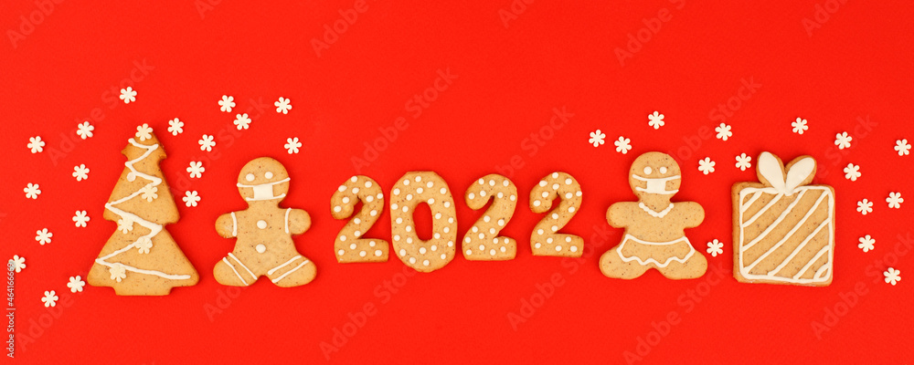 Happy New Year's set of numbers 2022, gingerbread man in face mask from ginger biscuits glazed sugar icing decoration on red background, minimal seasonal pandemic winter holiday banner