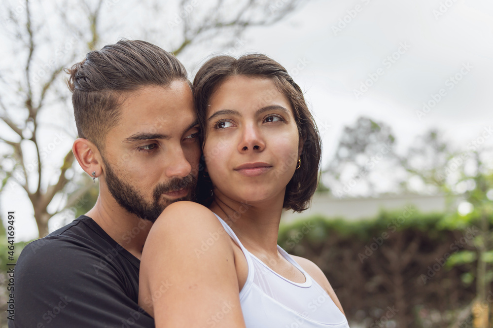 A boyfriend in love hugging girlfriend from back while she is looking away A boyfriend in love hugging girlfriend from back while she is looking away