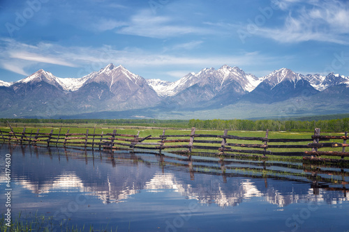 The mountains of the Eastern Sayan Mountains are reflected in the water. Landscape with a wooden fence. Buryatia, Russia