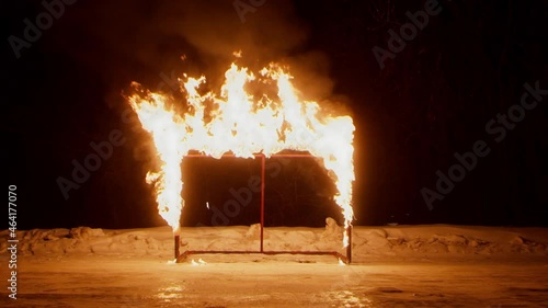 Carcass of hokey gate in large burning flame standing on empty ice arena with bank of snow at dark winter night photo