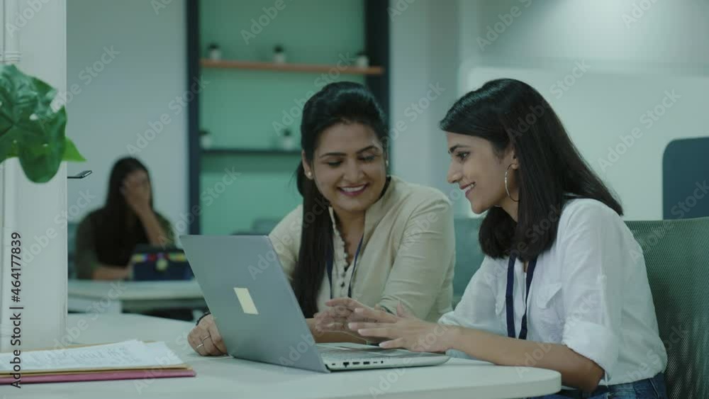 Two Indian businesswomen sitting in the office while talking together and using a laptop computer.Good looking Asian girls smiling and discussing about project on laptop in a start up business firm. Two Indian businesswomen sitting in the office while talking together and using a laptop computer.Good looking Asian girls smiling and discussing about project on laptop in a start up business firm.