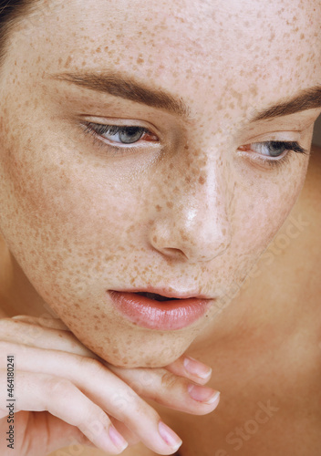 Young beautiful girl with freckles, perfect skin and nude makeup touched her face
