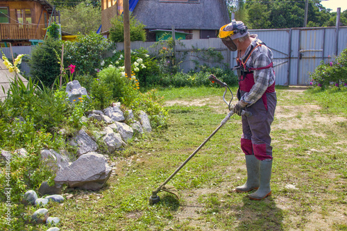 Aged man in overalls with a lawn mower mows the lawn. The gardener cares for the garden. photo